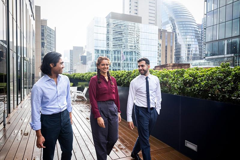 three employees walking on patio, Sydney office buildings in the skyline.