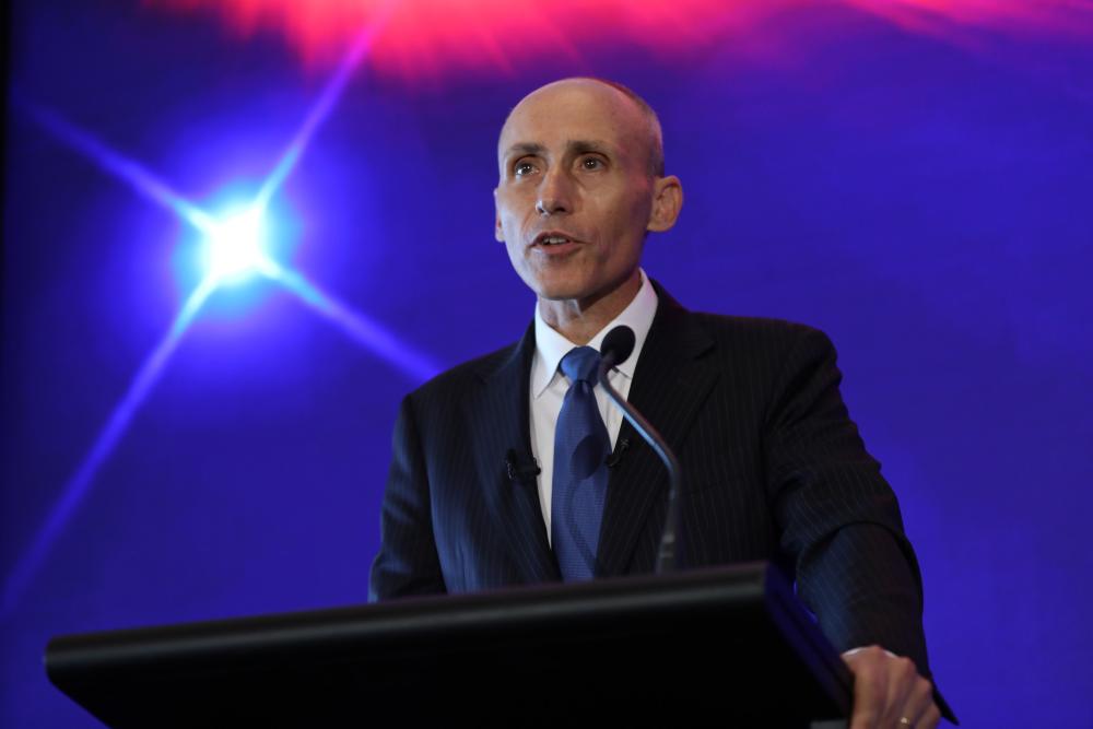 David Bradbury delivering a speech at a lectern with a brighly coloured background.