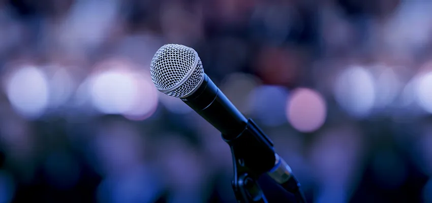 Close-up of a microphone against a blurred, colorful background, creating a vibrant, anticipatory mood, suggesting an upcoming speech.